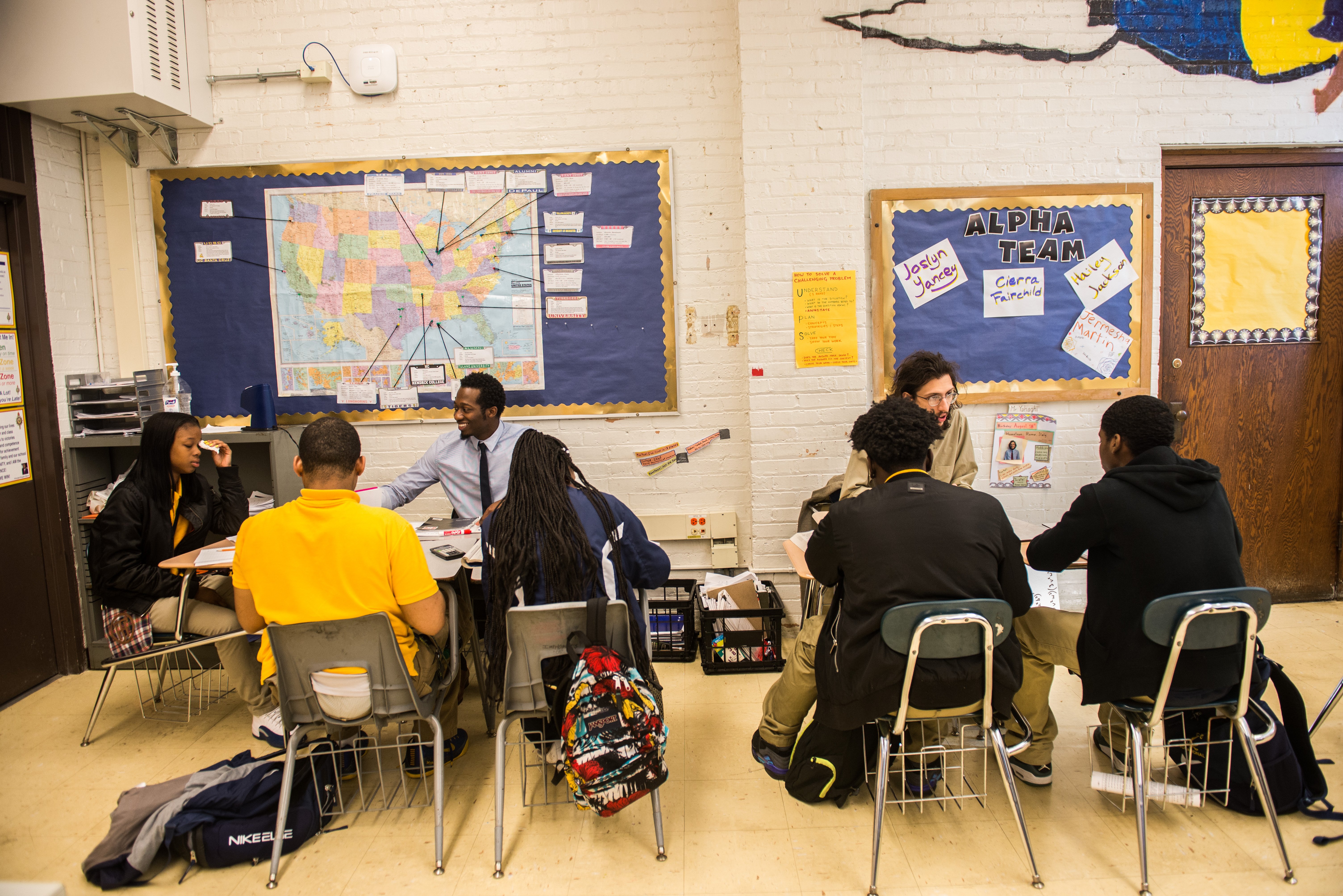 Two small groups of students in a classroom sitting at in grouped desks led by a math tutor 