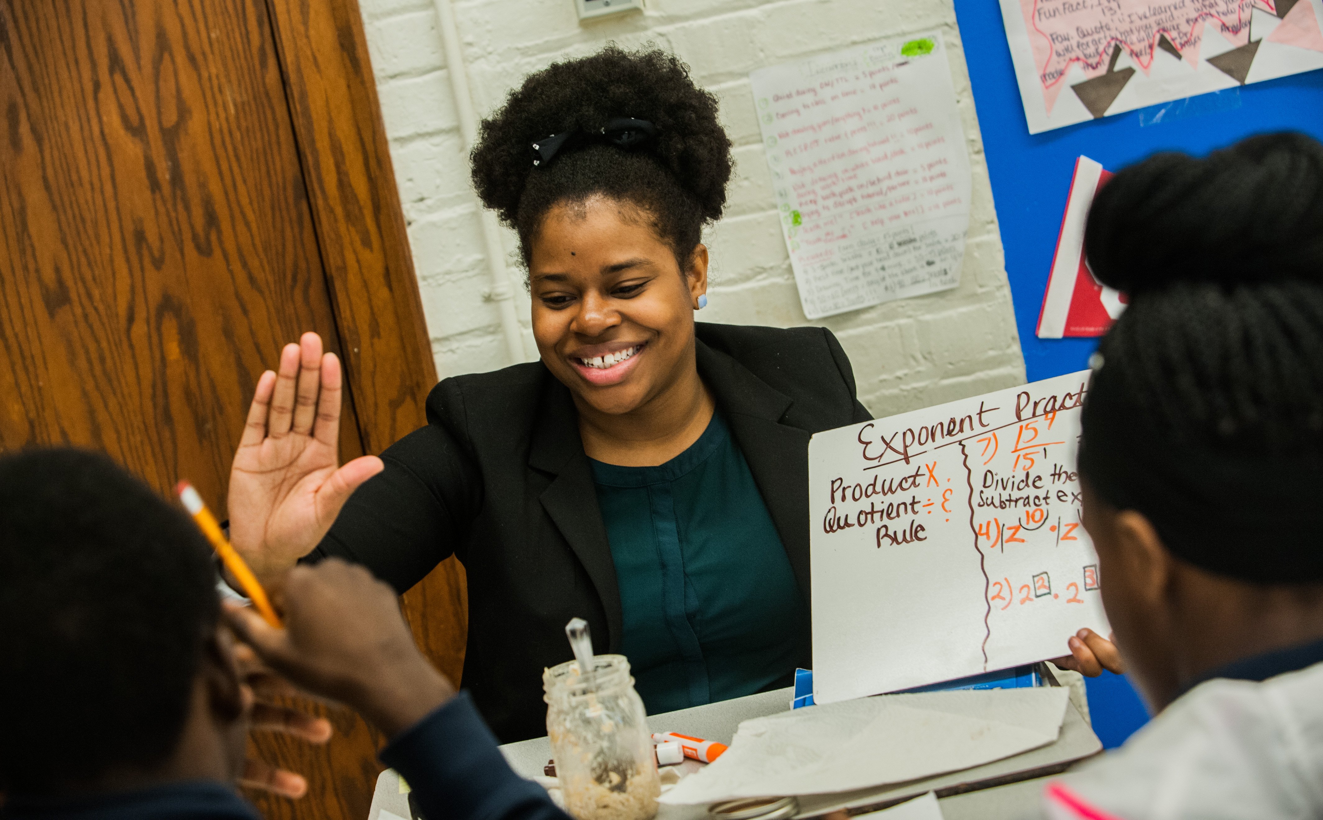 Smiling tutor holding a small whiteboard with math problem offers a high-hive to student