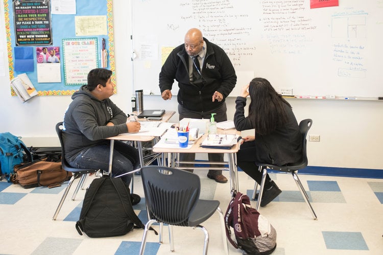 Standing tutor talks to students at desk to explain math